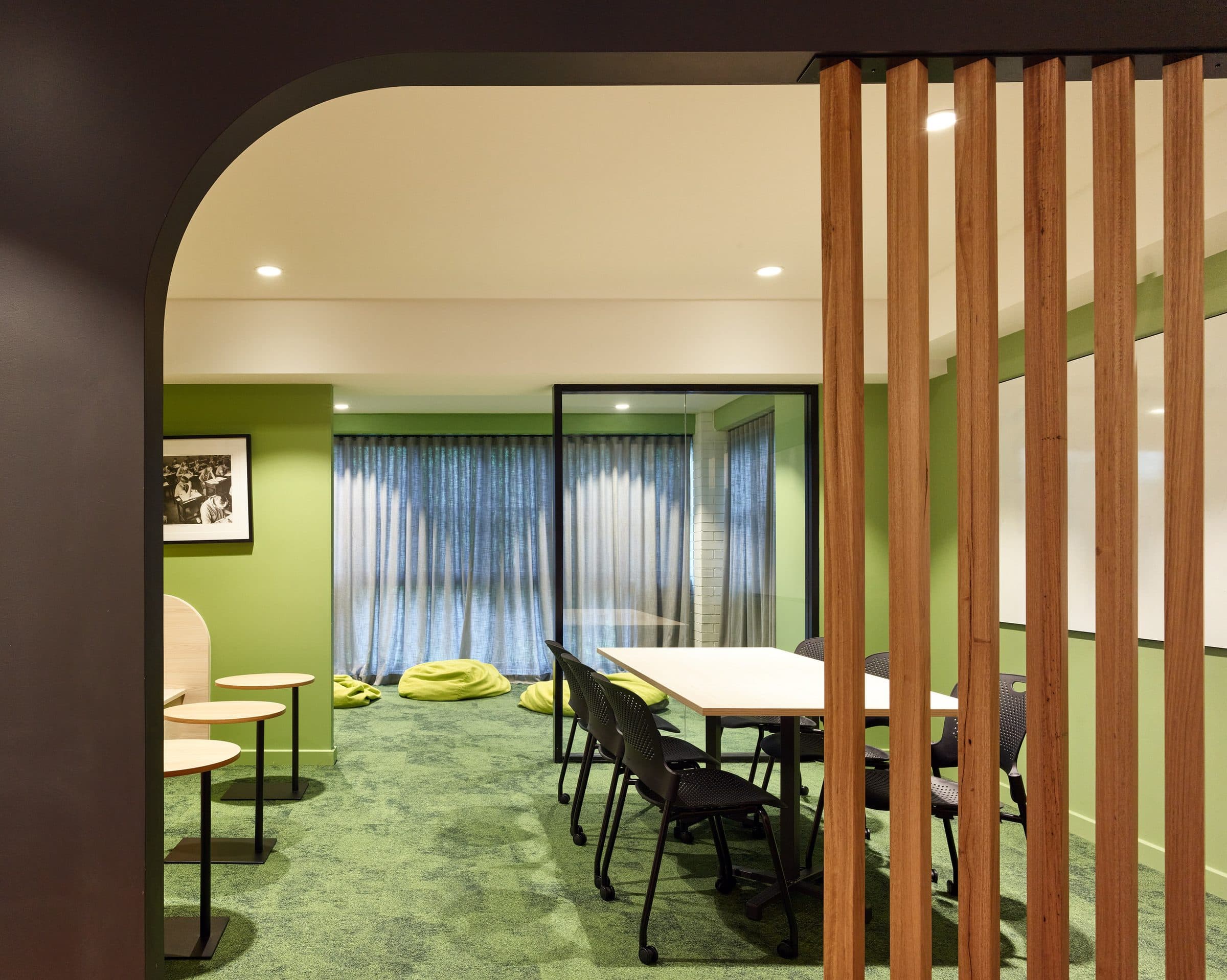 Study room behind timber battens with green carpet and long tables.