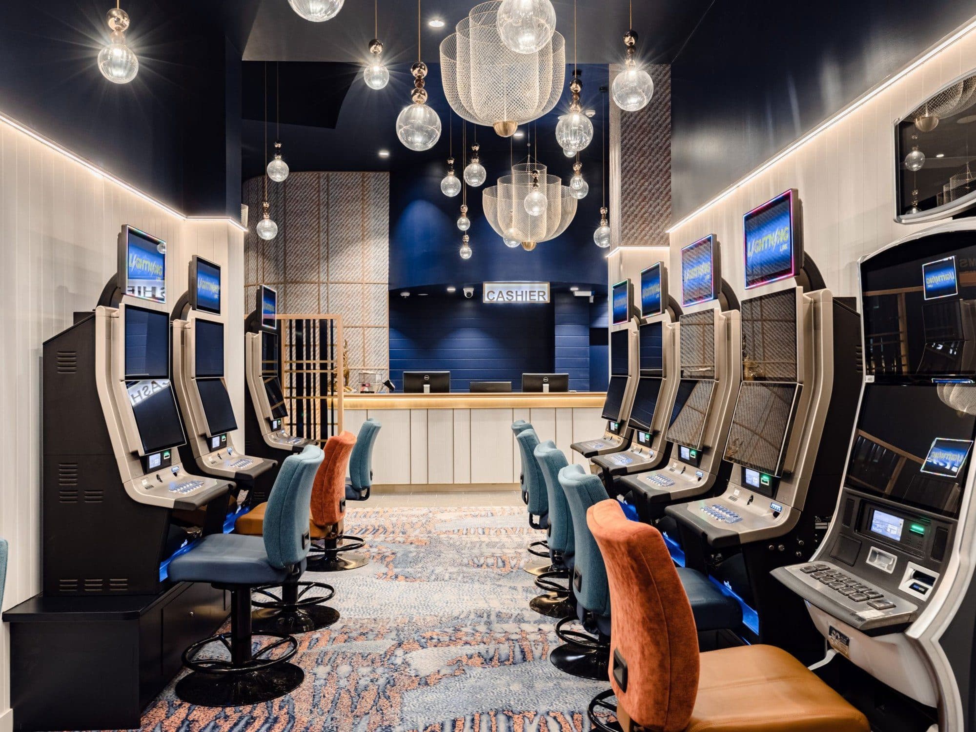 Rows of gaming machines under clusters of glass pendants.