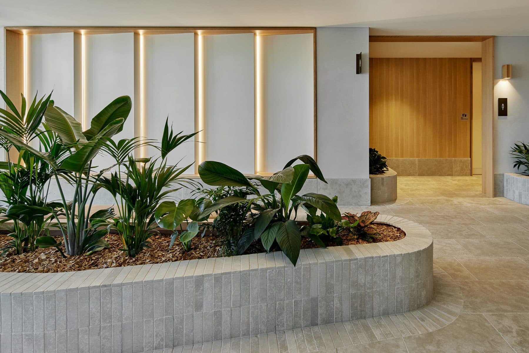 The clubhouse breezeway, with a curved stone planter under timber battens and a backlit screen wall.