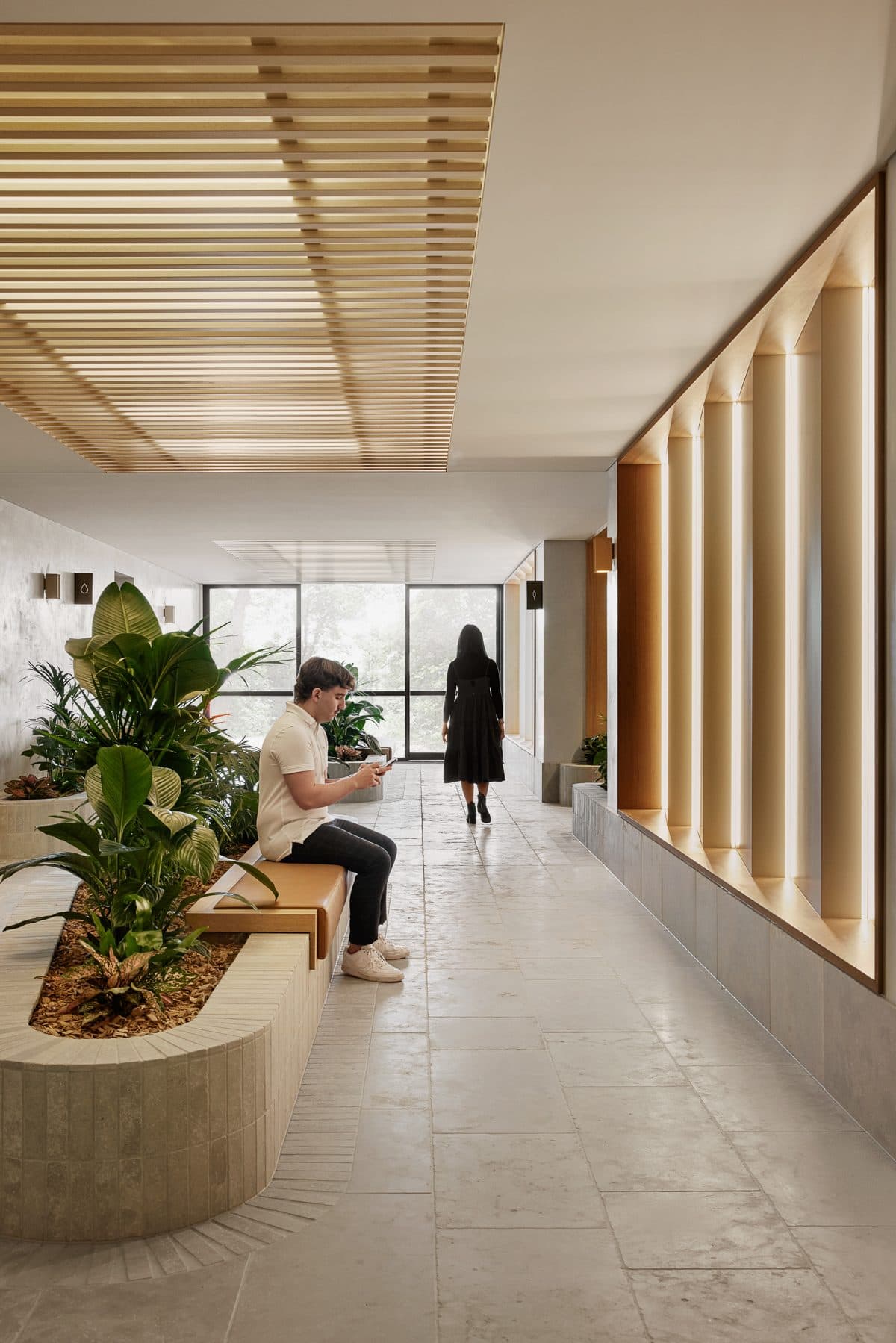 Members seated beside a planter in the breezeway, with backlit timber panels behind.