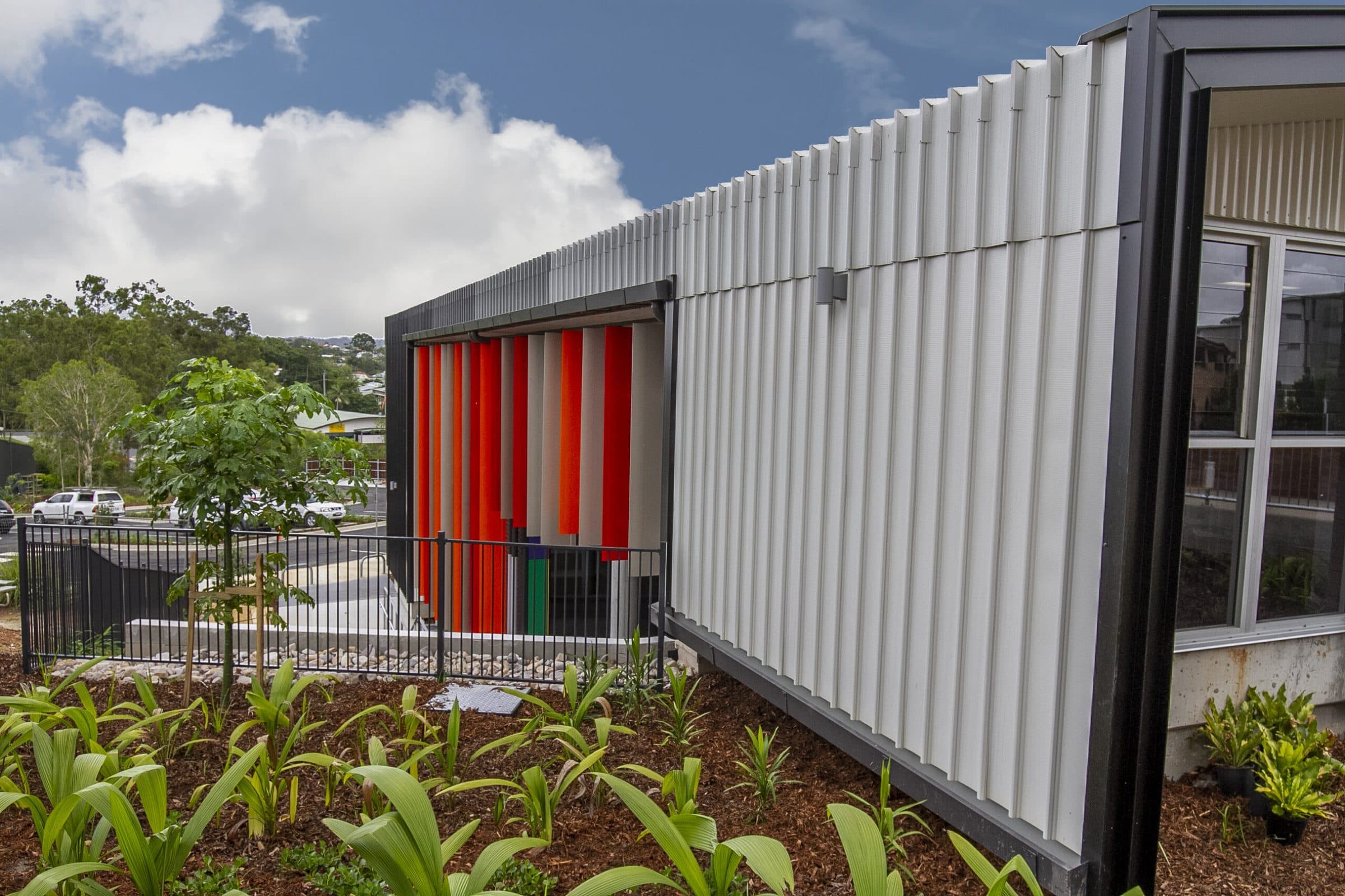 The fins and white ribbed cladding on the side of the building, with new planting.