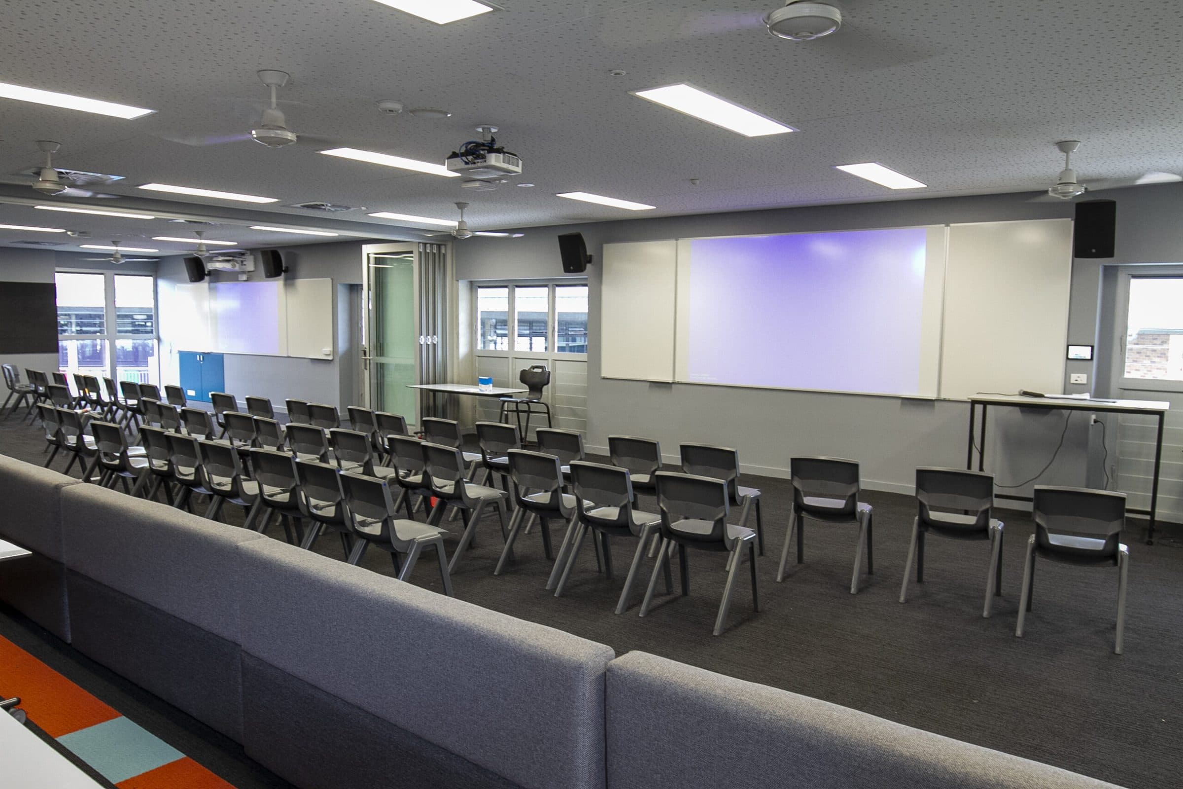 A large learning space with tiered seating, projection screens and loose chairs.