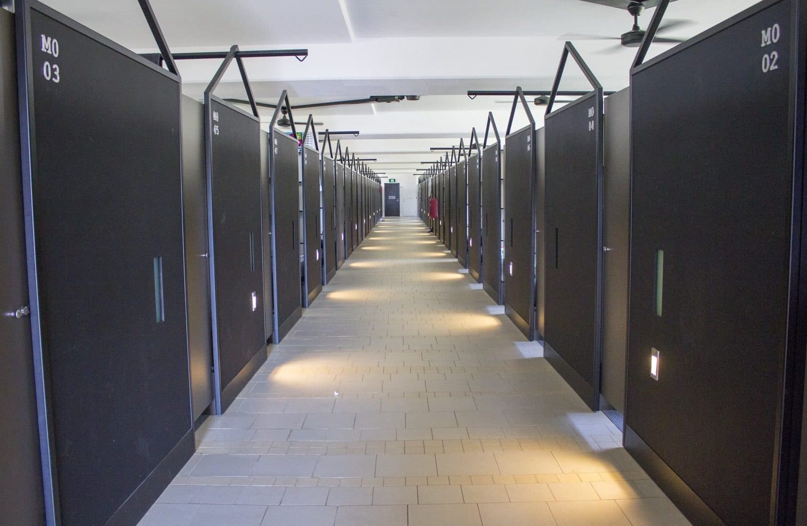 A boarding corridor lined with dark sleeping-room doors under a pitched steel frame.
