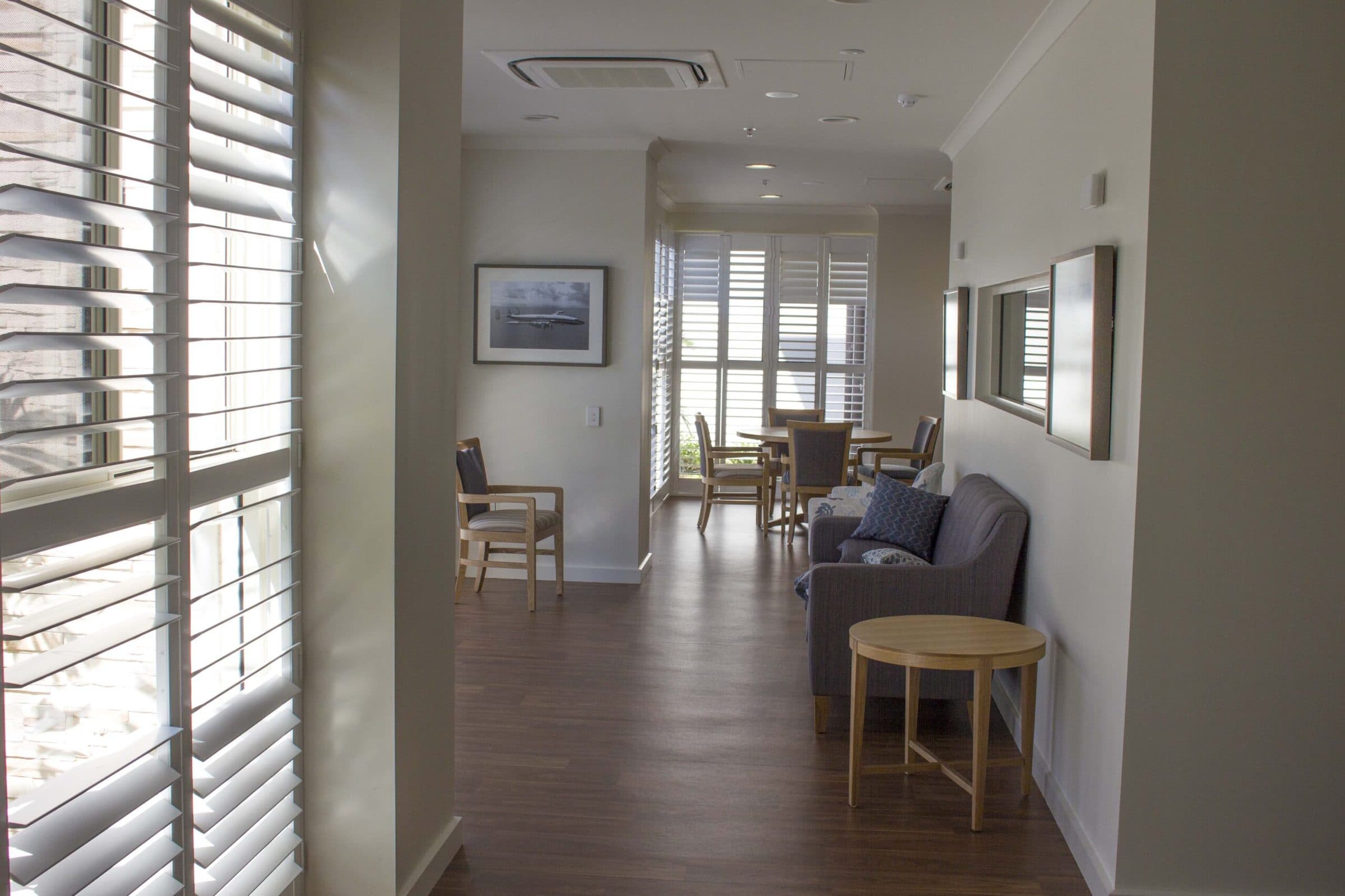A resident sitting area by plantation shutters, with timber-look flooring.