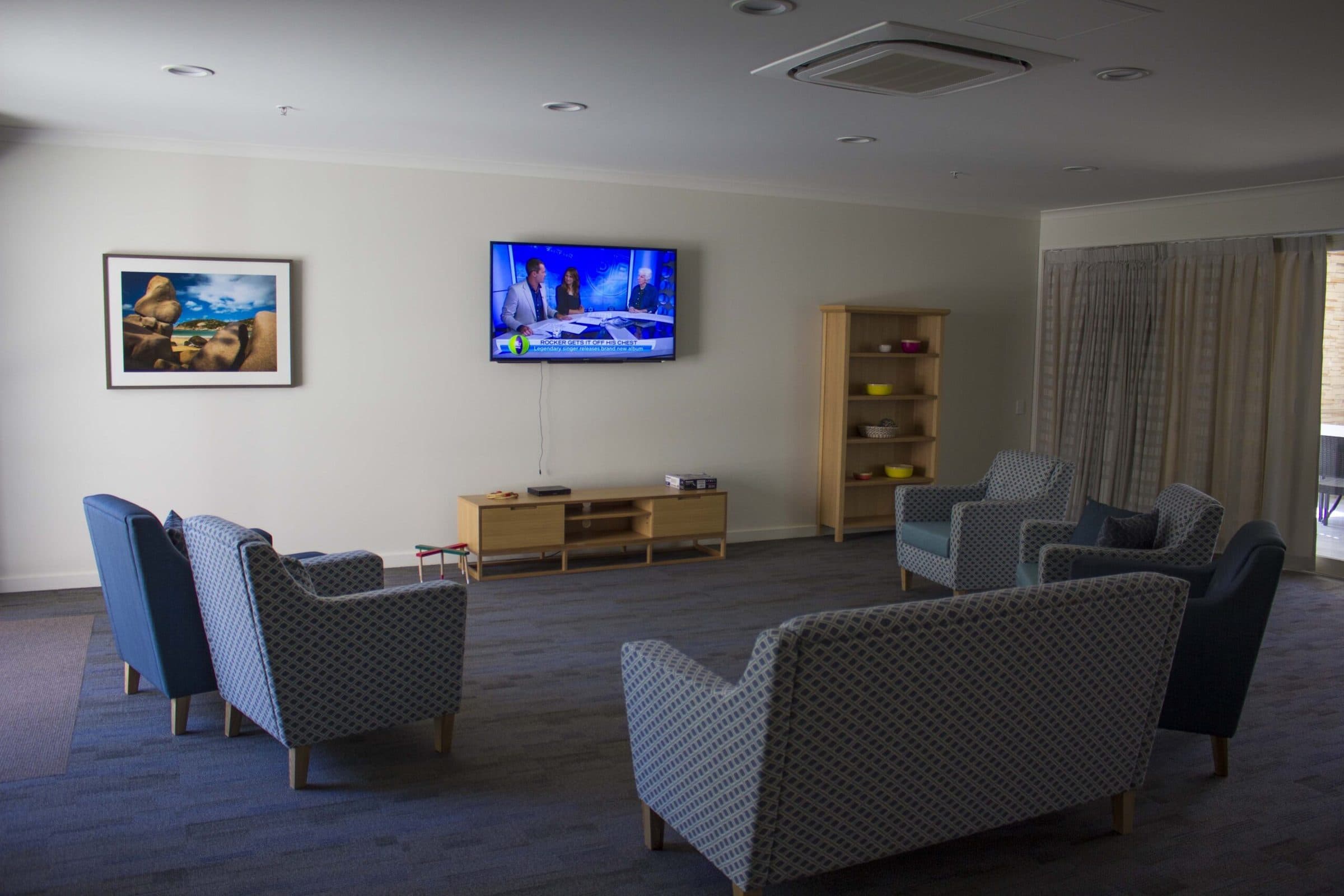 A resident lounge with armchairs and a wall-mounted television.