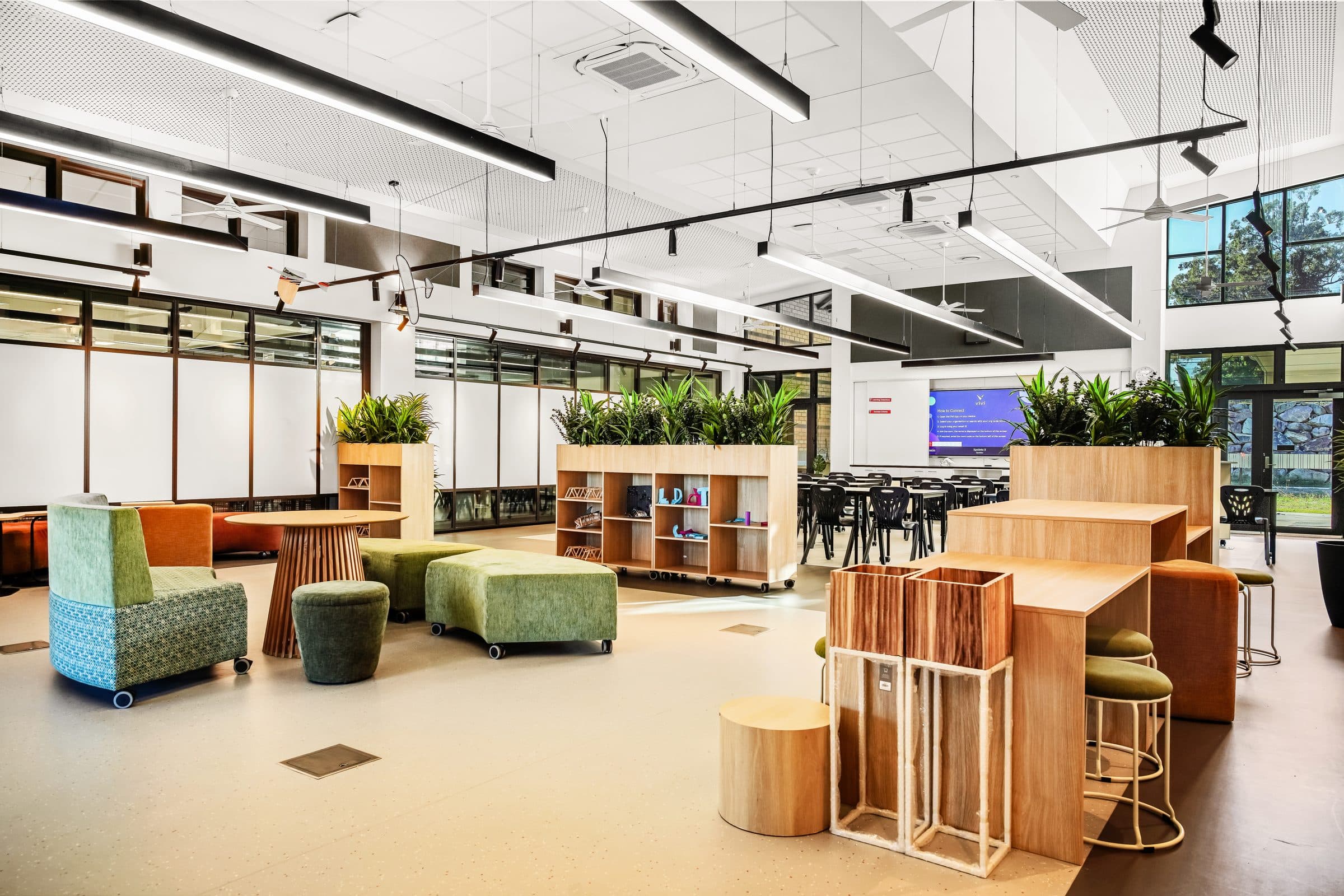 A learning space with soft seating, planter shelving and tables along the glazing.